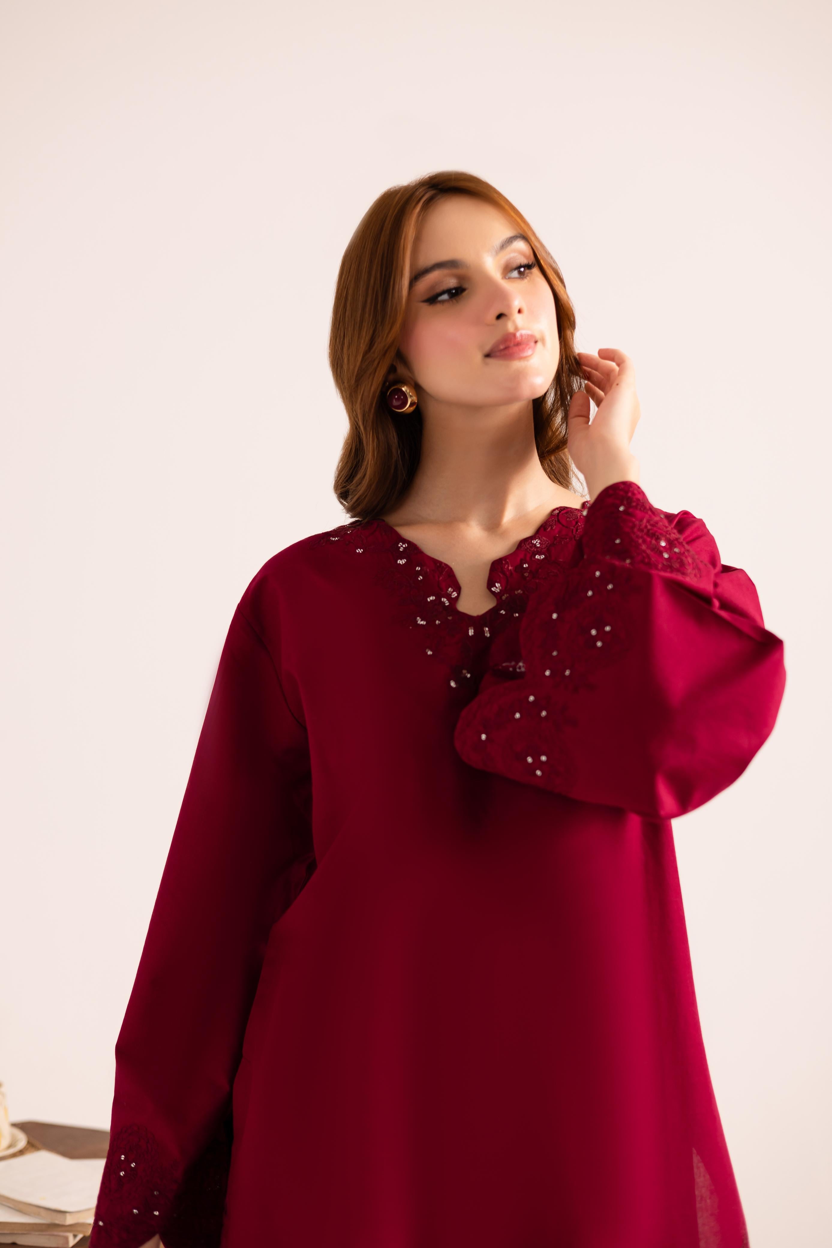 Woman wearing a burgundy dress with embellishments on a light background